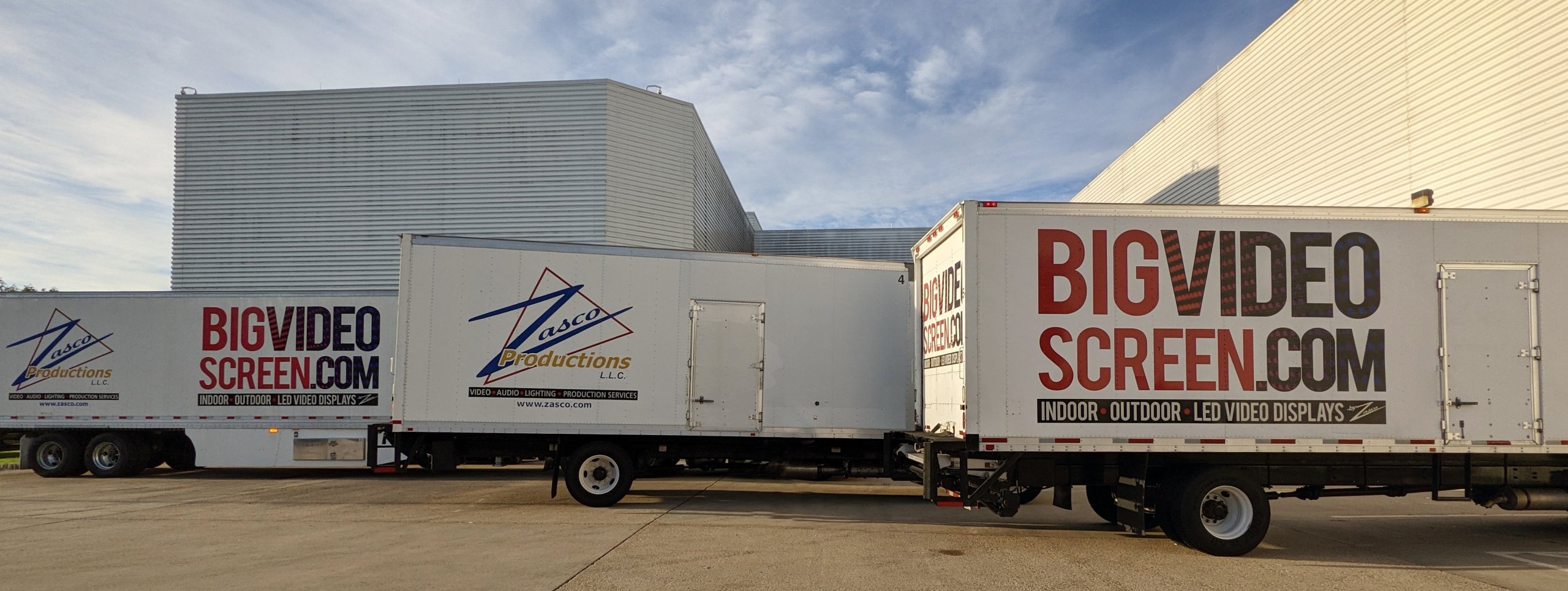 Three trucks with Zasco and BigVideoScreen logos parked outside a venue