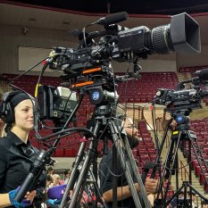 Broadcast camera on tripod with operator at arena event