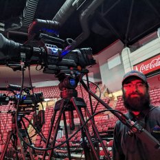 Broadcast camera on tripod with operator at arena event